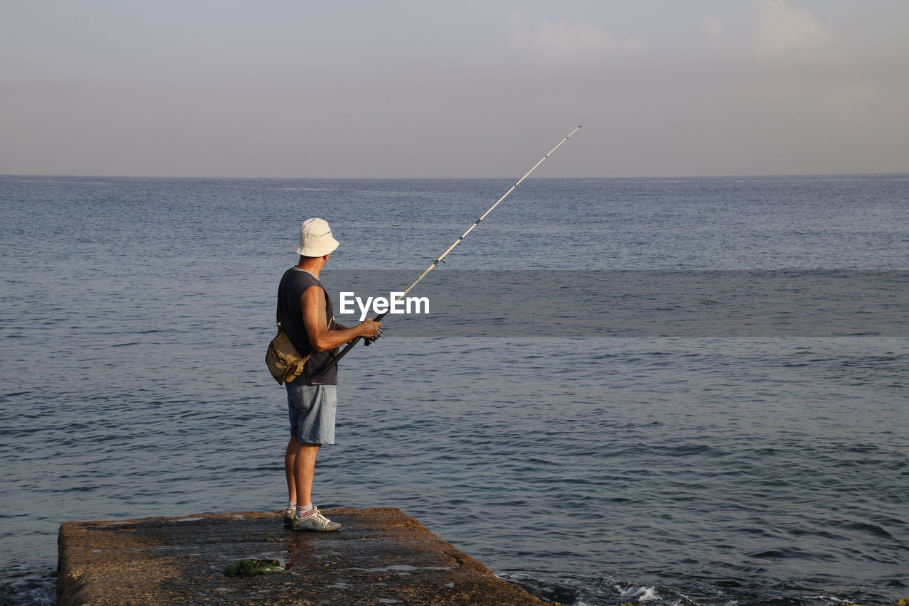 Man fishing on concrete jetty in sea against sky