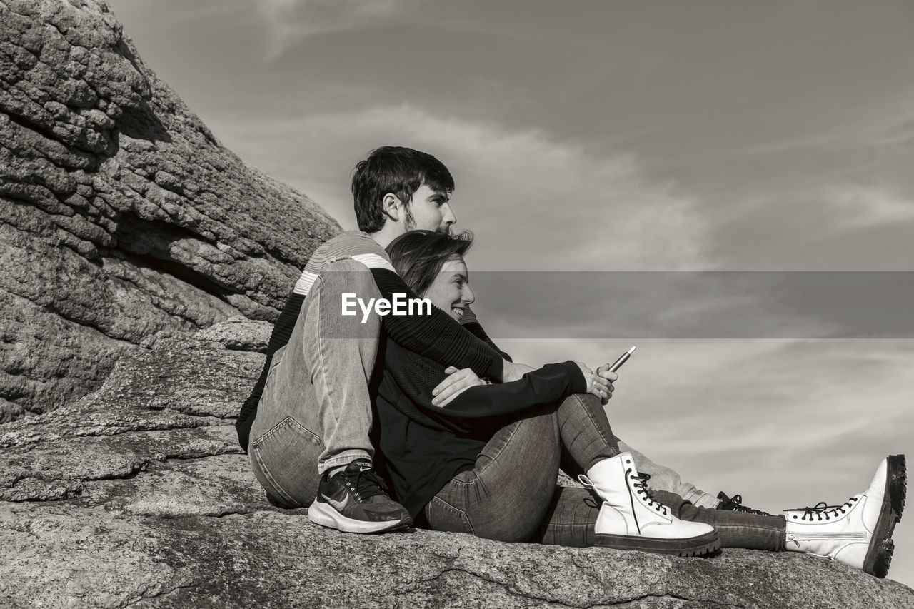 sky, sitting, one person, black, white, full length, nature, cloud, rock, adult, leisure activity, relaxation, black and white, monochrome, activity, men, lifestyles, monochrome photography, footwear, casual clothing, young adult, outdoors, side view, mountain, photo shoot, day, land, looking, child, person