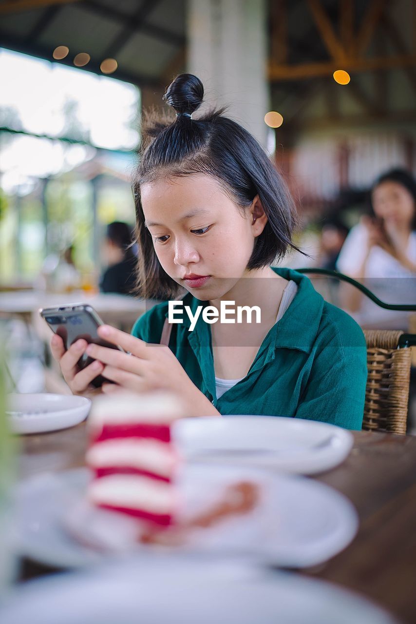 Teenage girl using phone at cafe