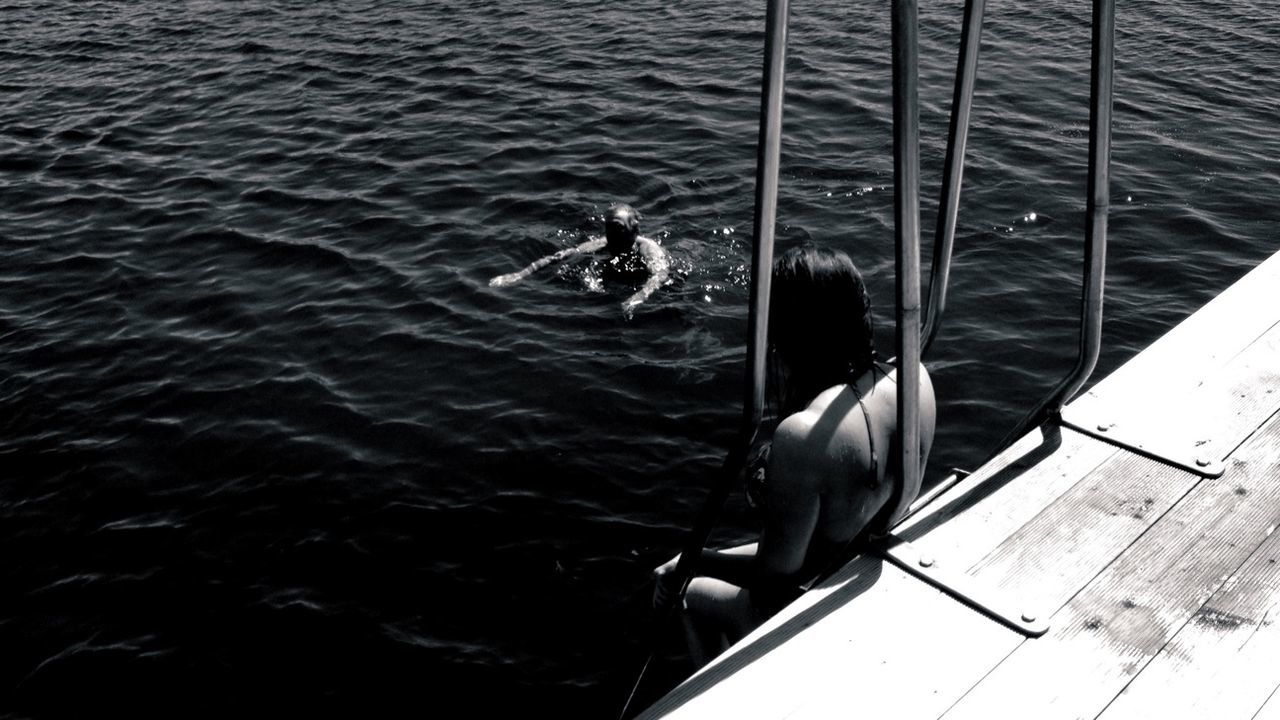 High angle view of woman on jetty and man swimming in sea