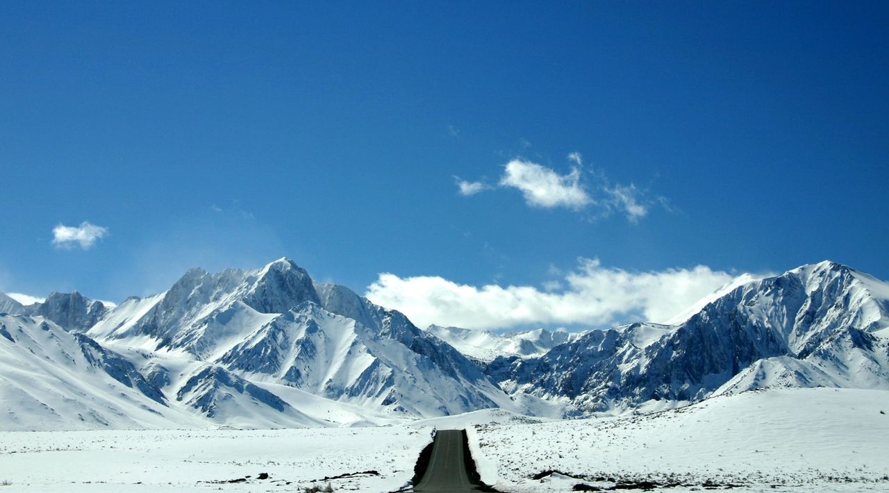 Empty road leading towards snowcapped mountain against sky