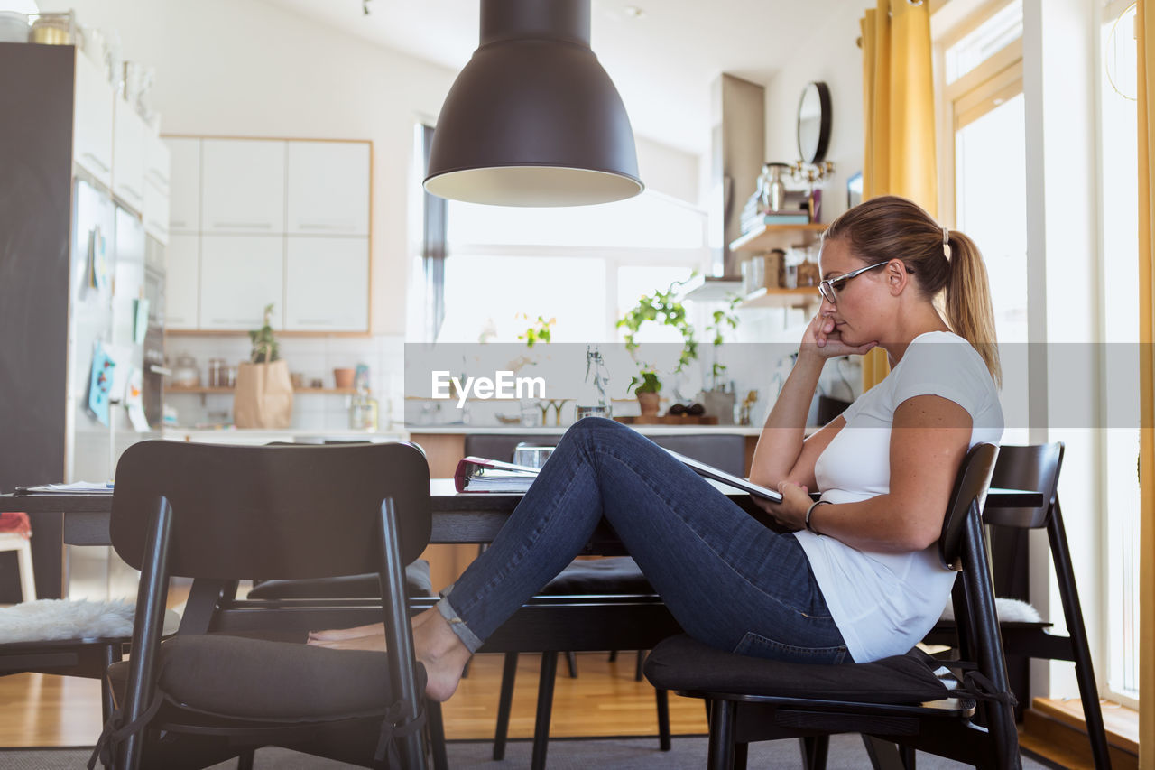 Side view of woman watching digital tablet while sitting on chair at home