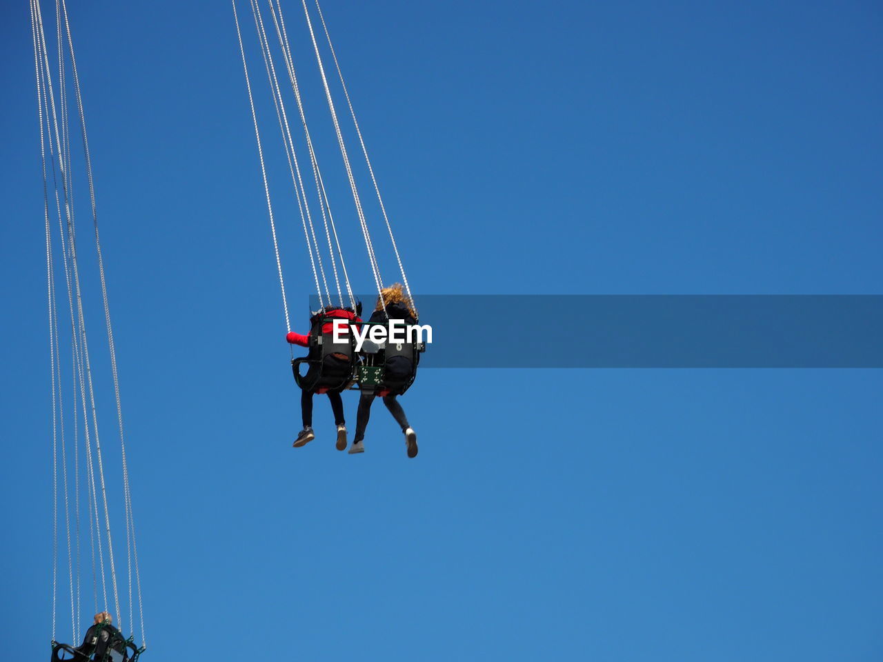 Low angle view of people enjoying in chain swing ride against clear sky