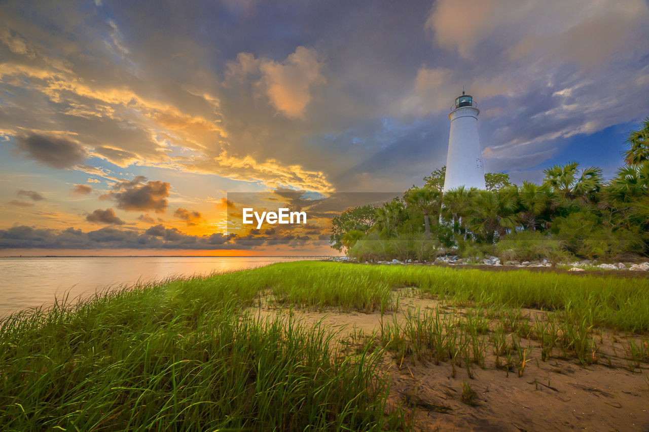 As the sun sets behind st. marks lighthouse, casting a warm glow over the grasses and palm trees.