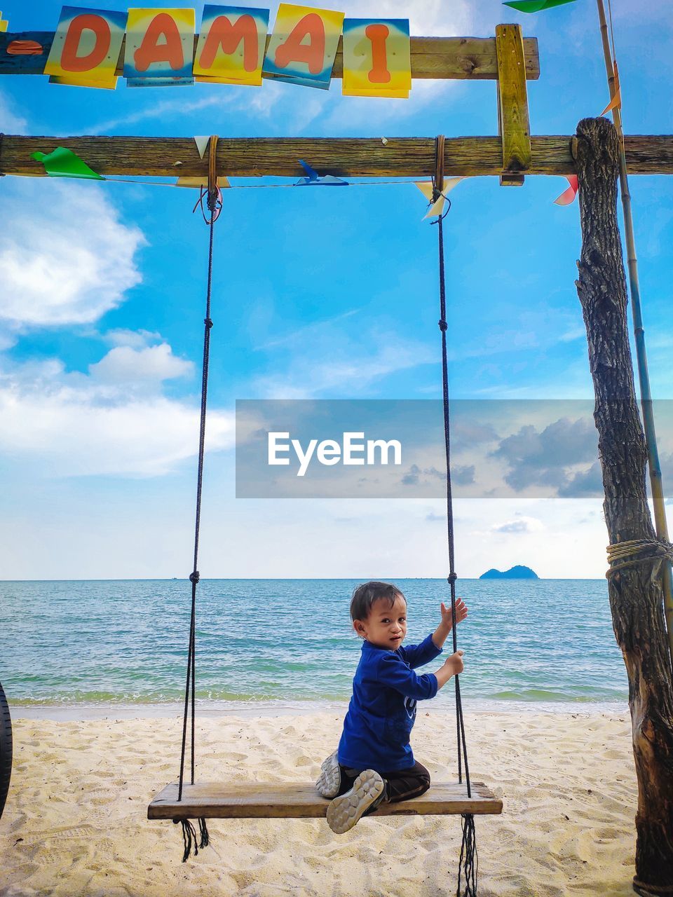Boy on swing at beach against sky