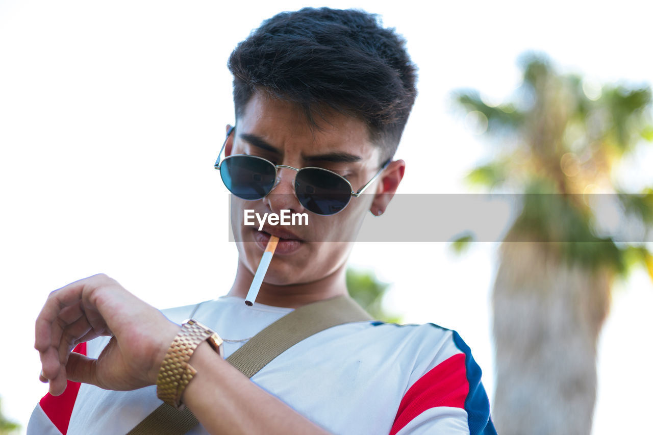 A young guy smoking a cigarette and wearing sunglasses