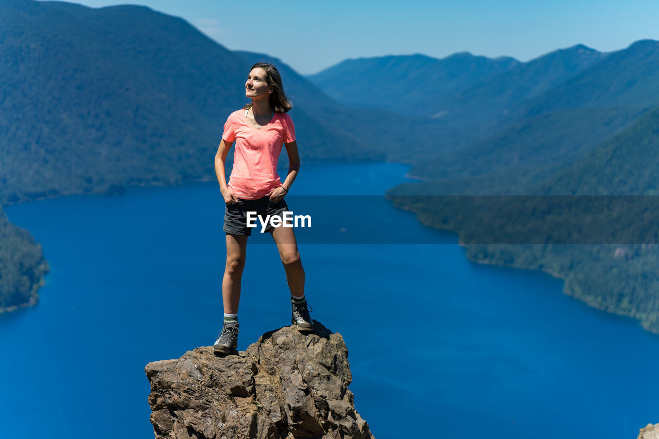 Hiker girl is on top of the mountain overlooking deep blue lake