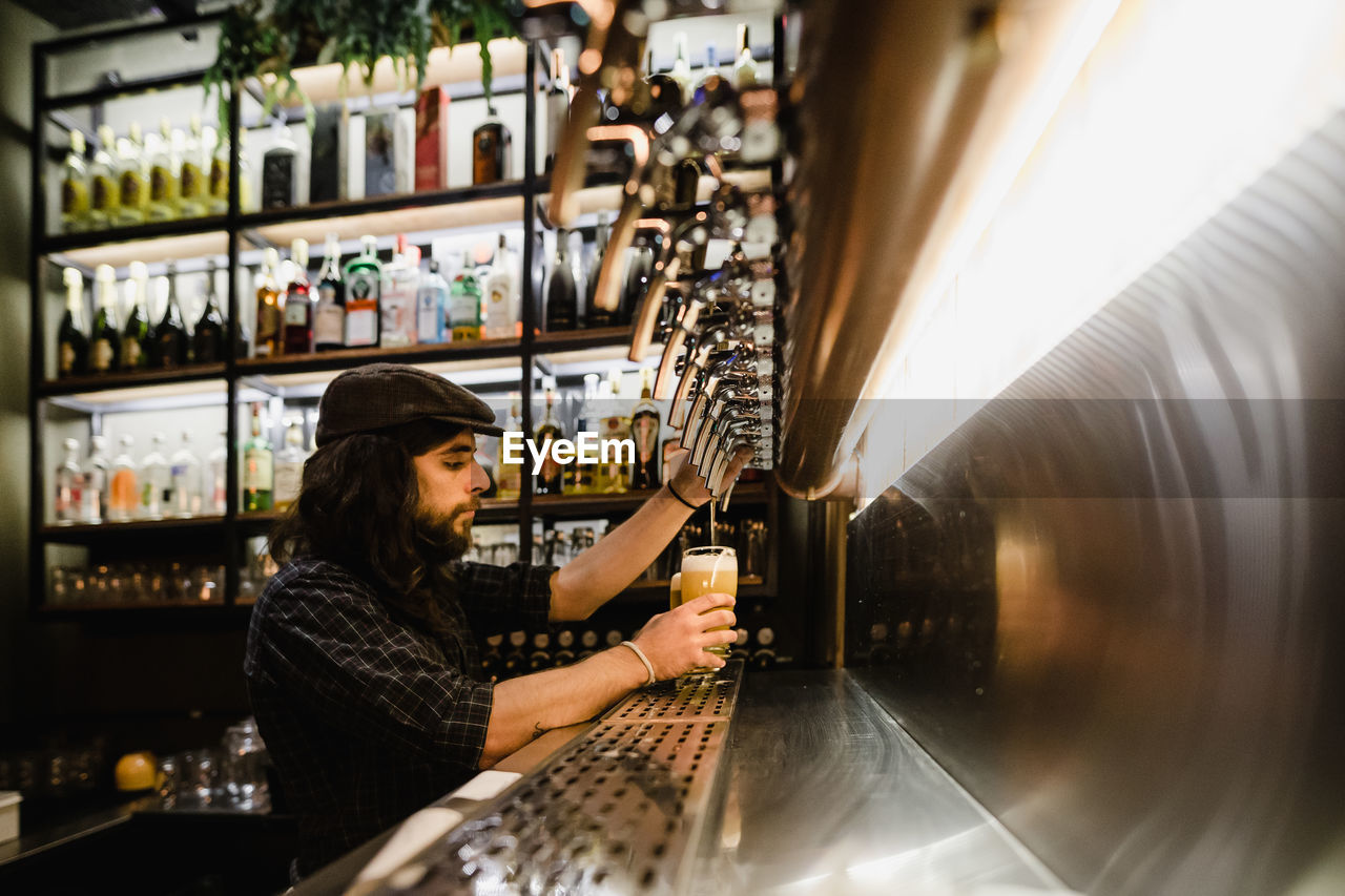 Side view of bartender filling beer glass at bar