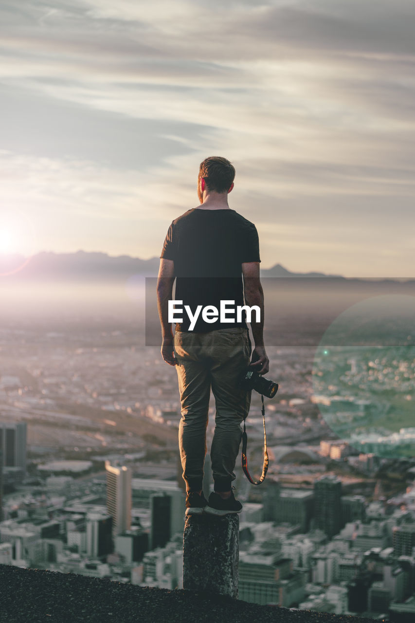 Full length of man with camera standing against cityscape during sunny day