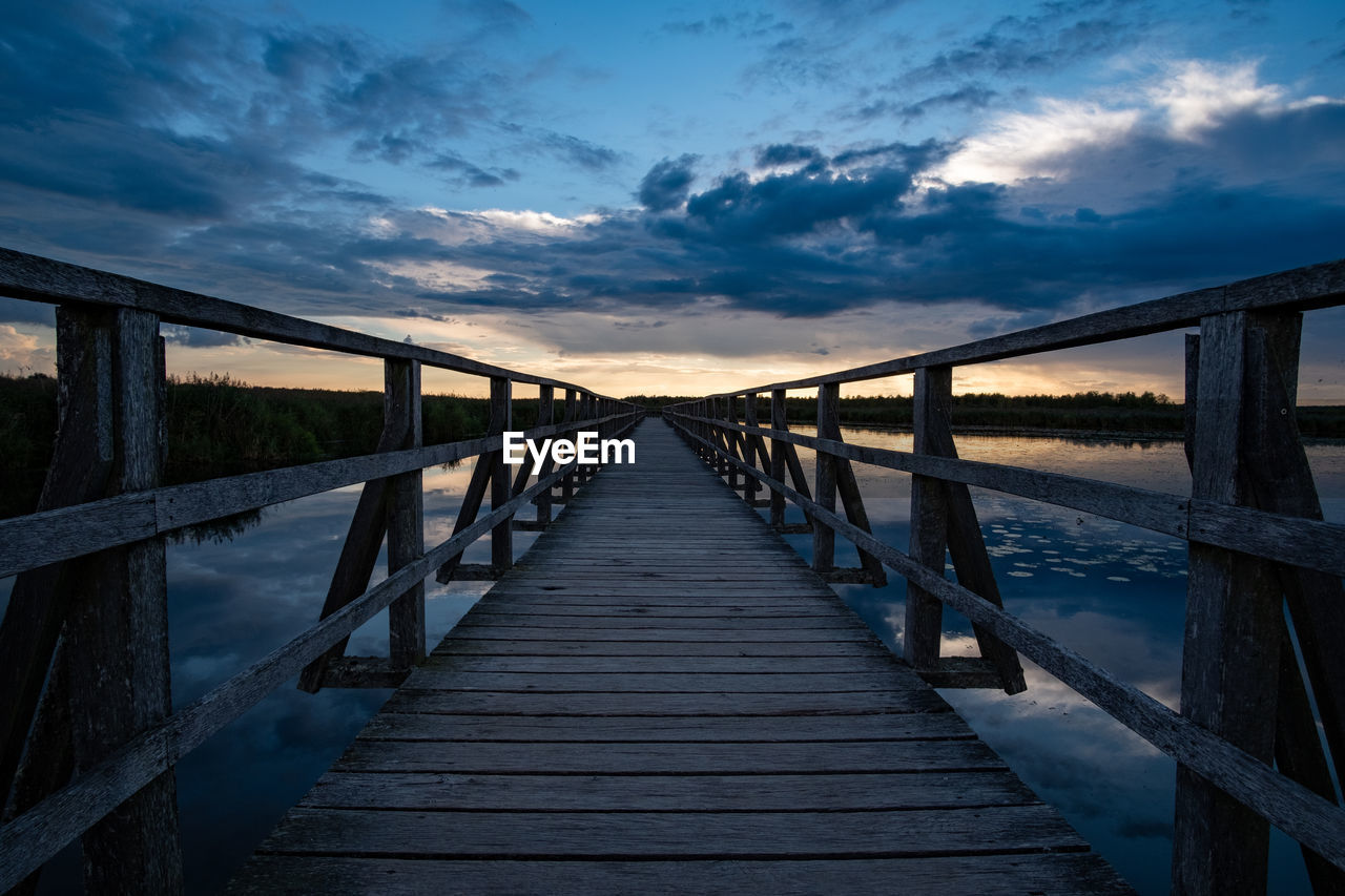 Footbridge over sea against sky during sunset