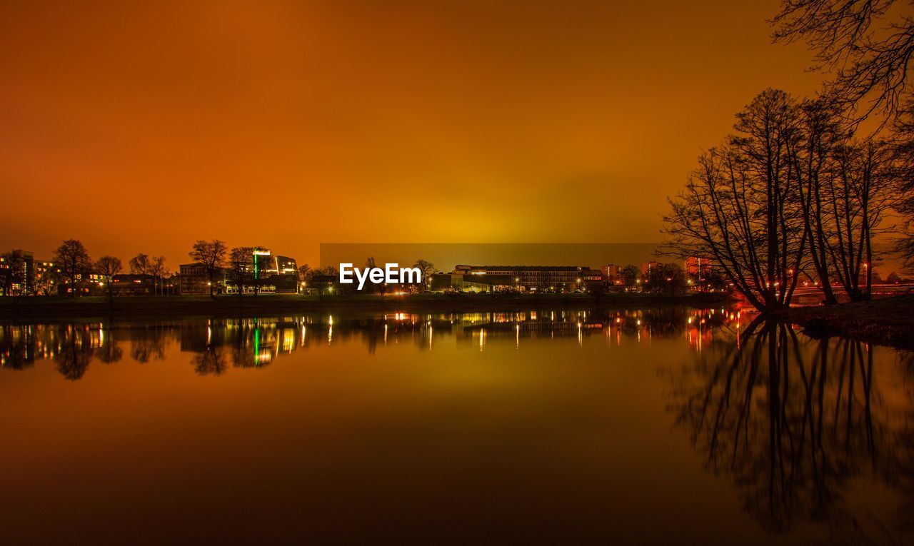 Reflection of illuminated buildings in lake against sky during sunset