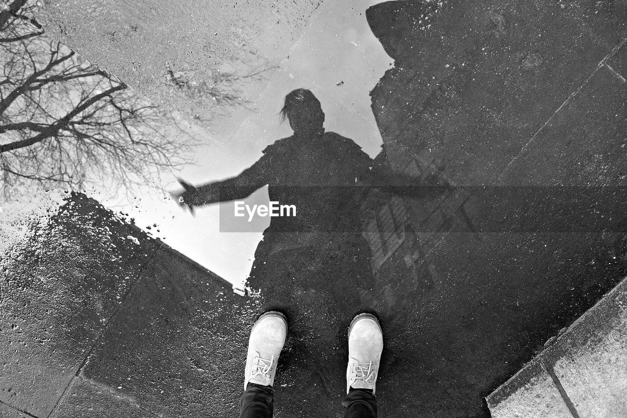 Low section of person standing by puddle on road