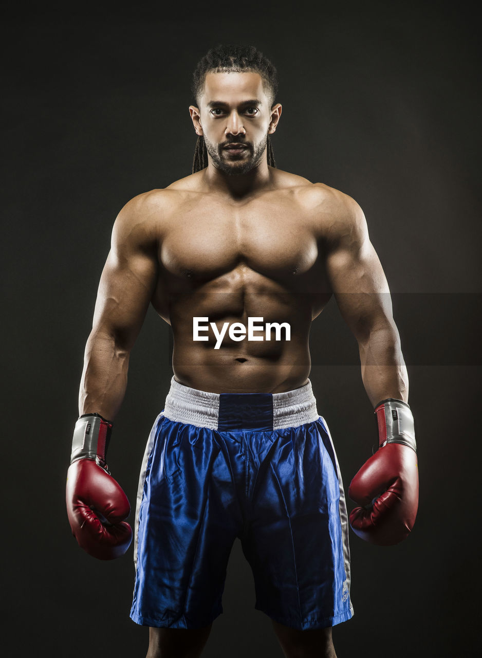 Portrait of shirtless boxer standing against black background