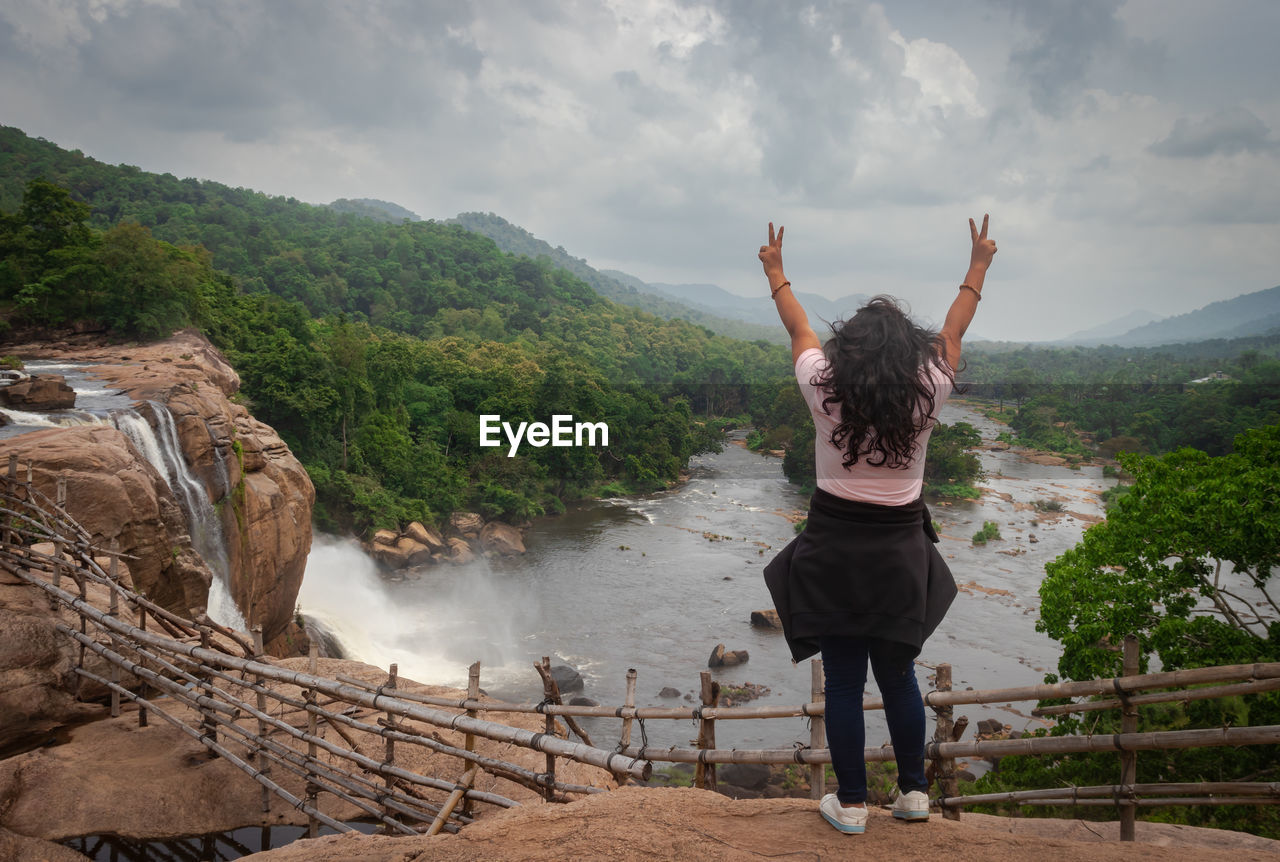 Girl solo traveler at waterfall with cloudy sky and green forests of the western ghat range