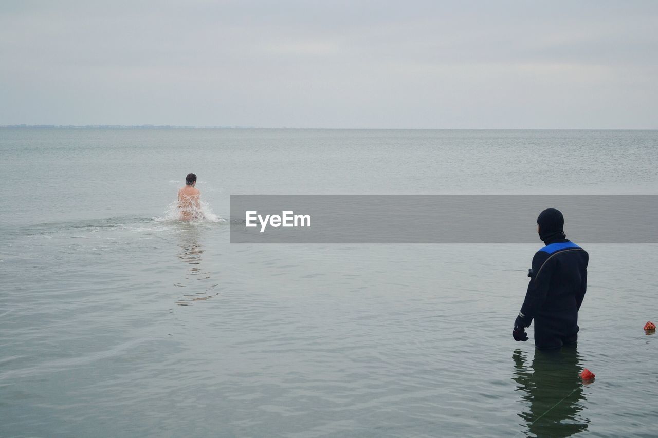 REAR VIEW OF MAN STANDING AT BEACH