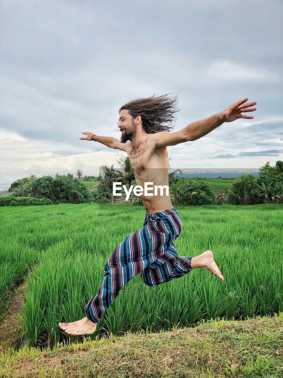 Shirtless man running on field against sky