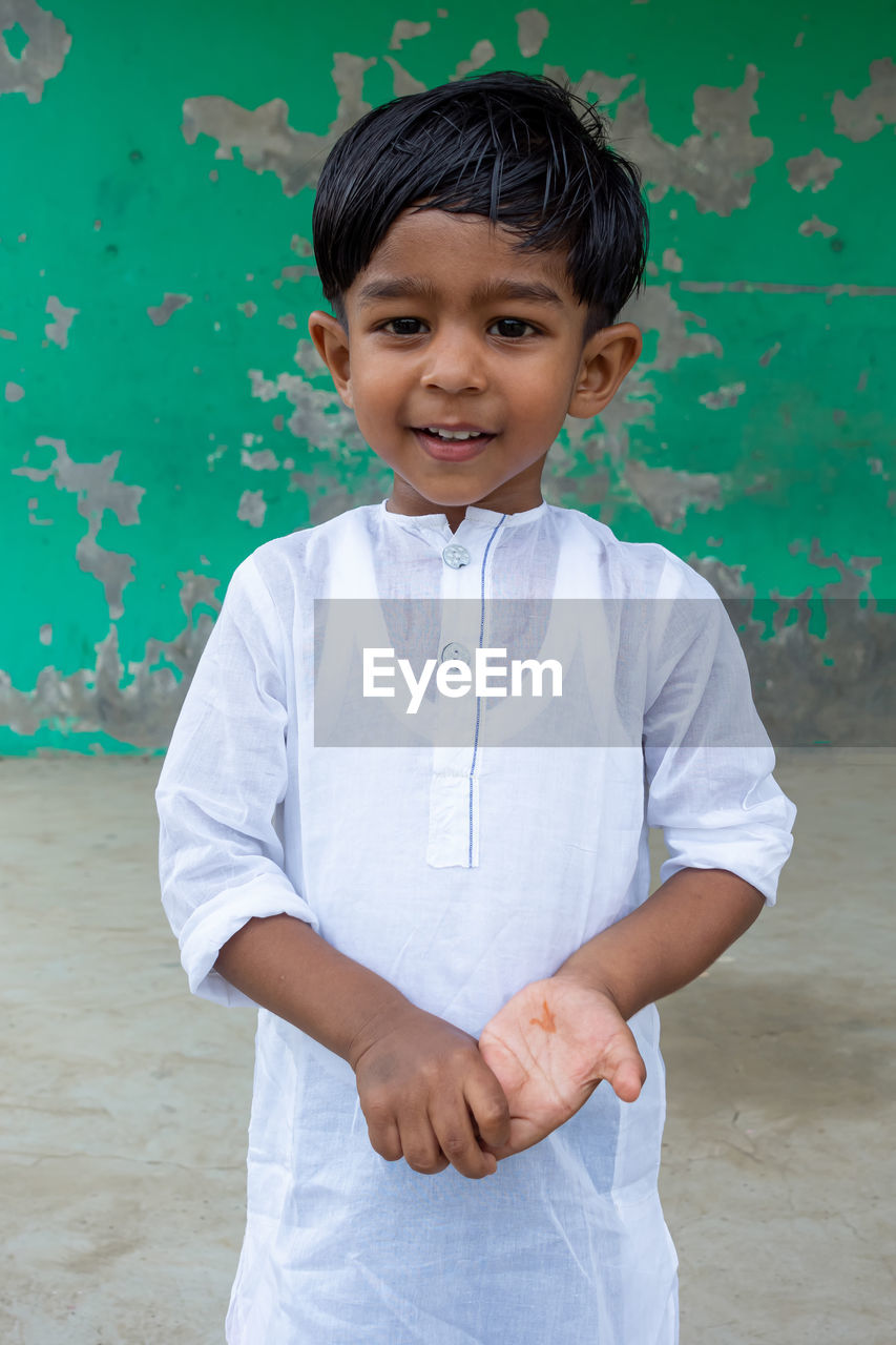 PORTRAIT OF SMILING BOY STANDING AGAINST WALL