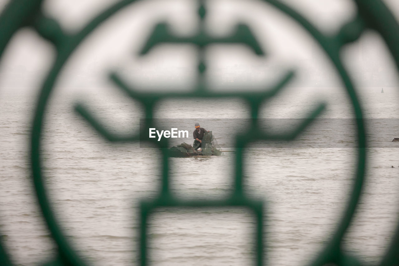 Fisherman fishing in sea seen through window