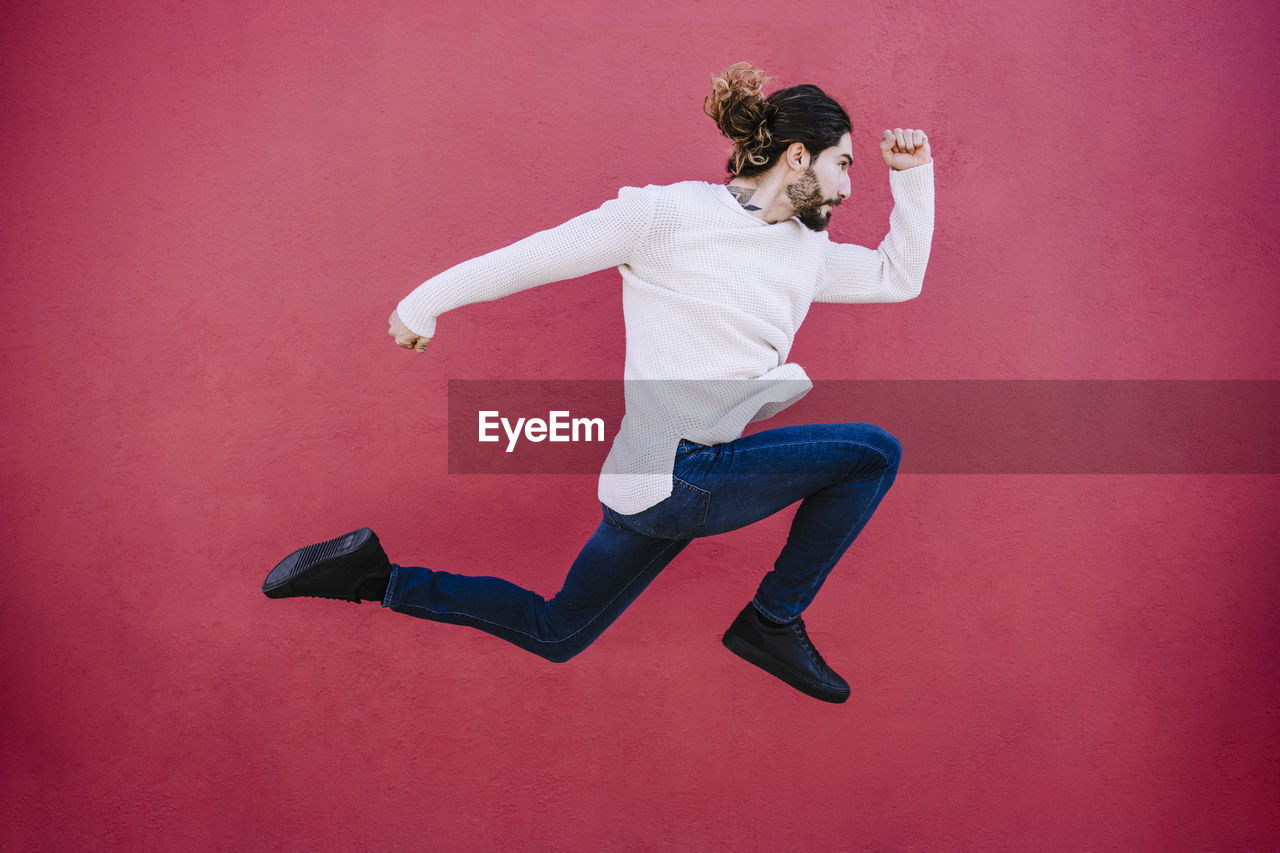 Young man running against red wall