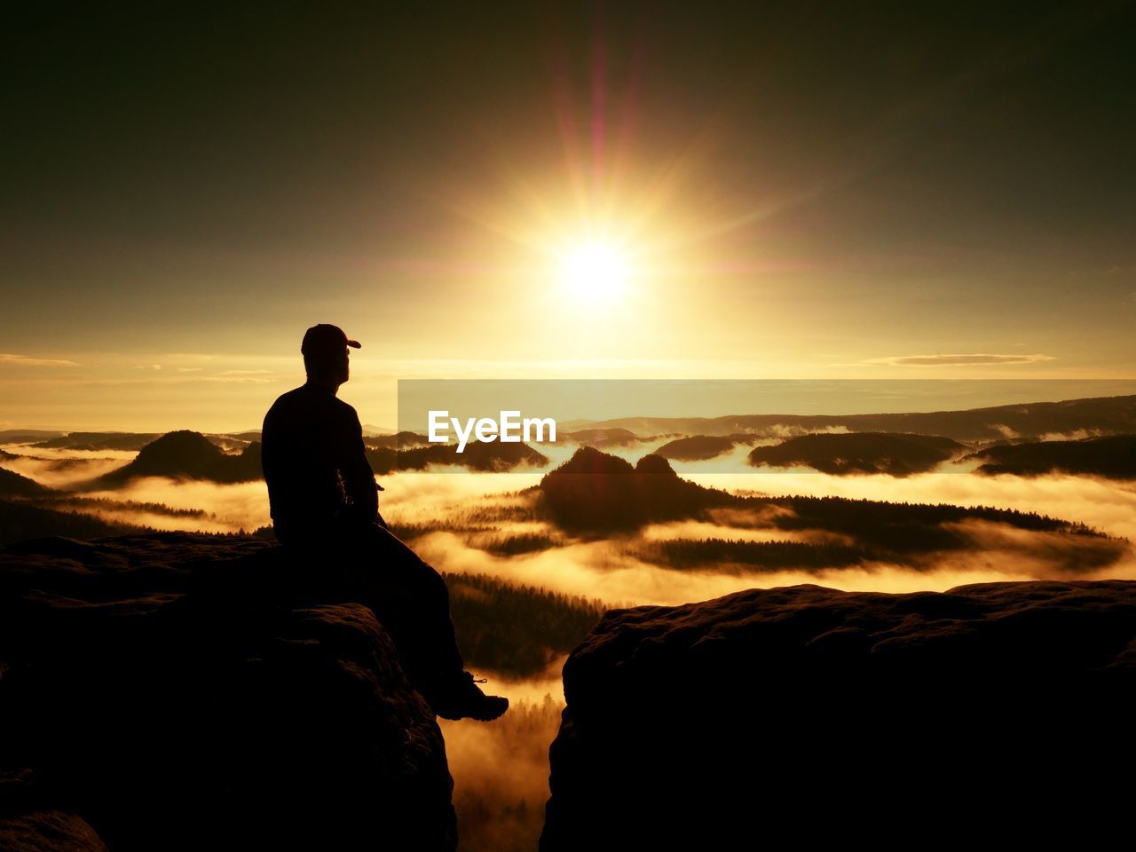 Moment of loneliness. man with cap sit on the peak of rock and thinking. dreamy autumn ladscape