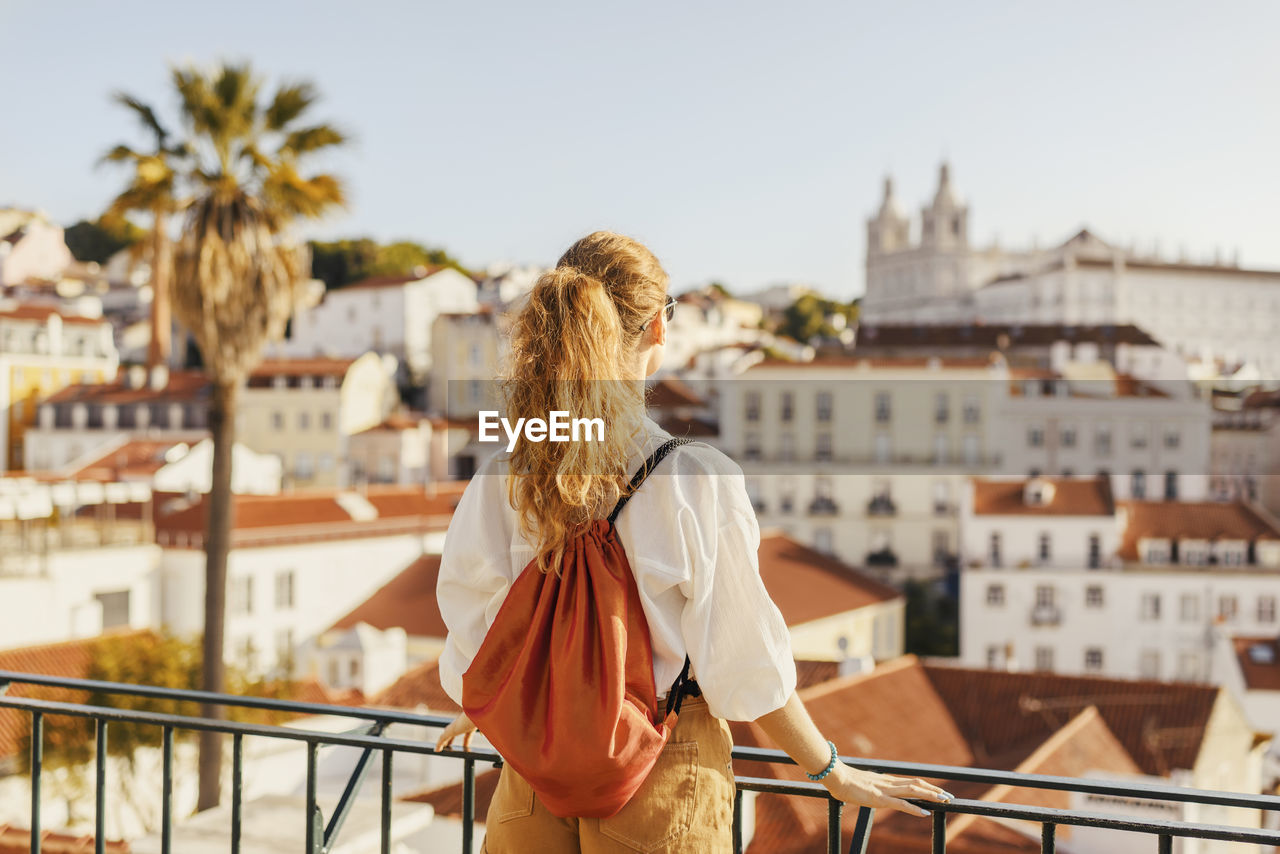 Rear view of woman standing by railing against buildings and sky