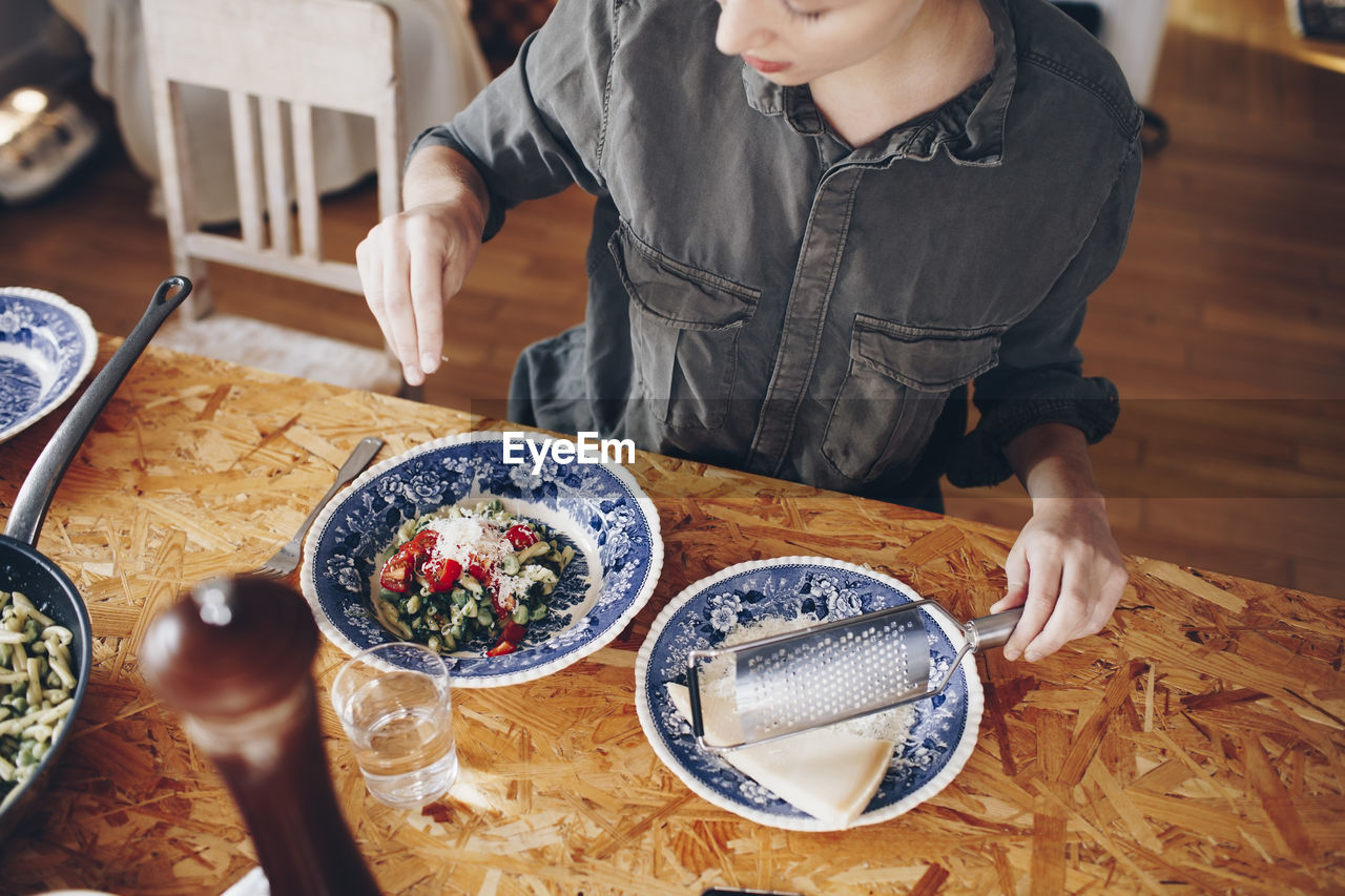 High angle view of woman sprinkling cheese on pasta in plate at home