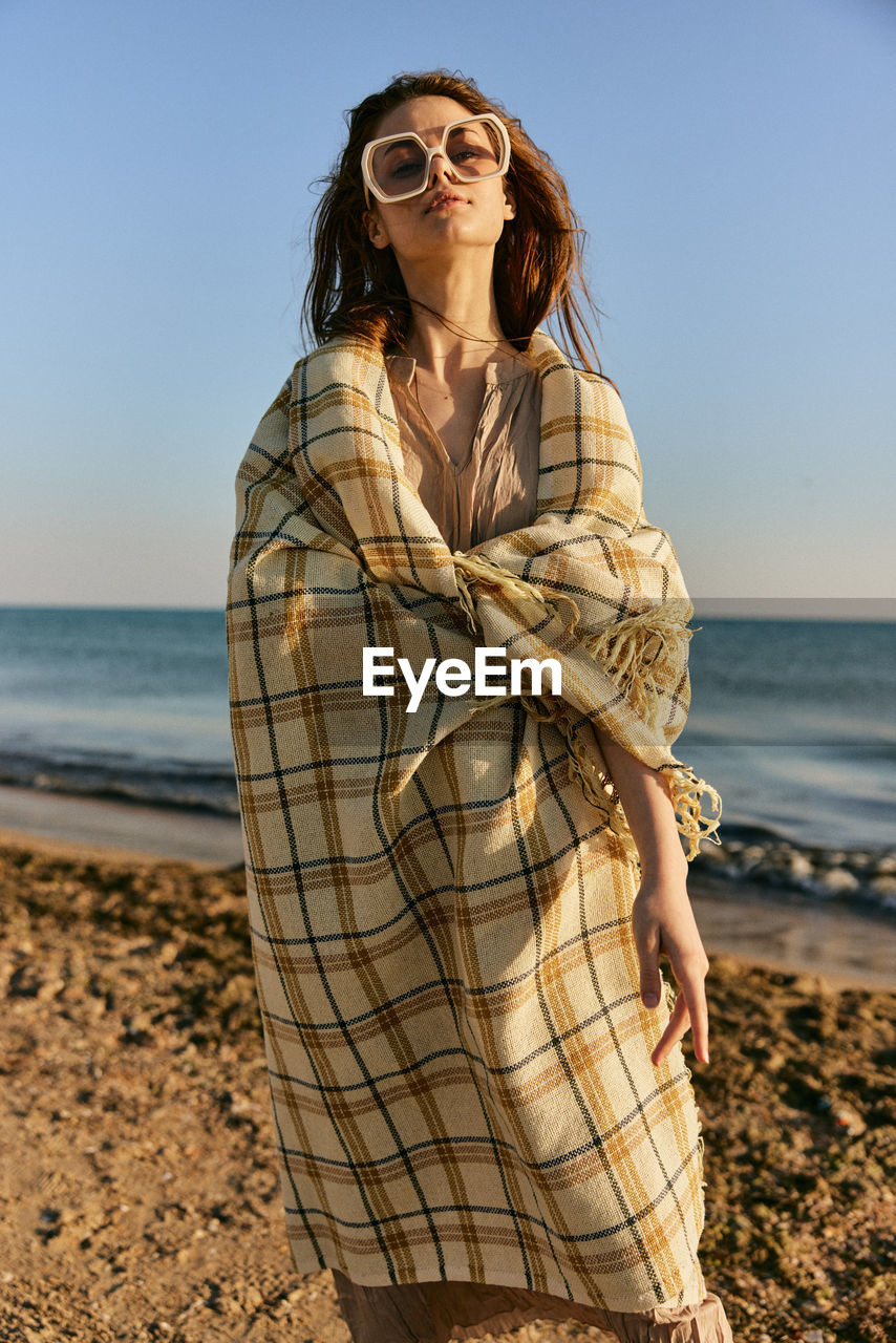 Young woman standing at beach against sky