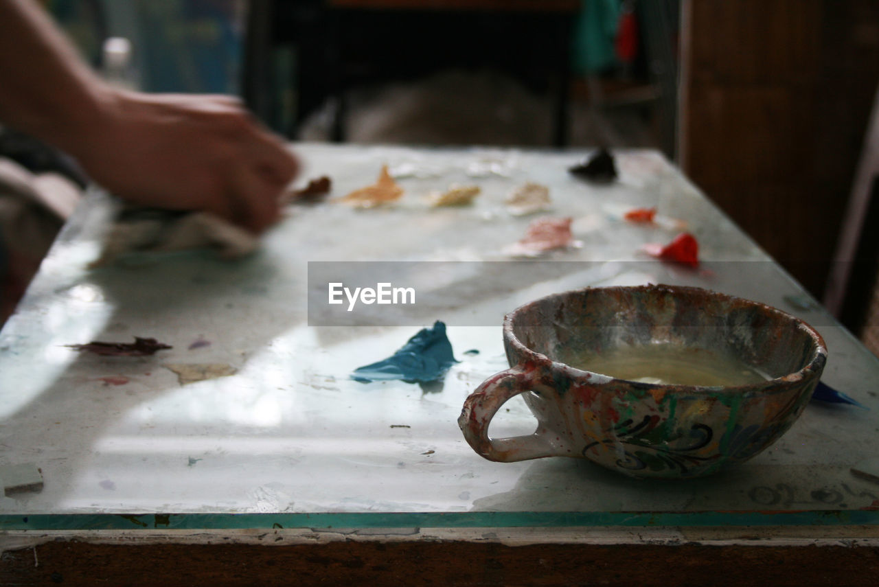 Cropped hand of painter working in studio with focus on cup