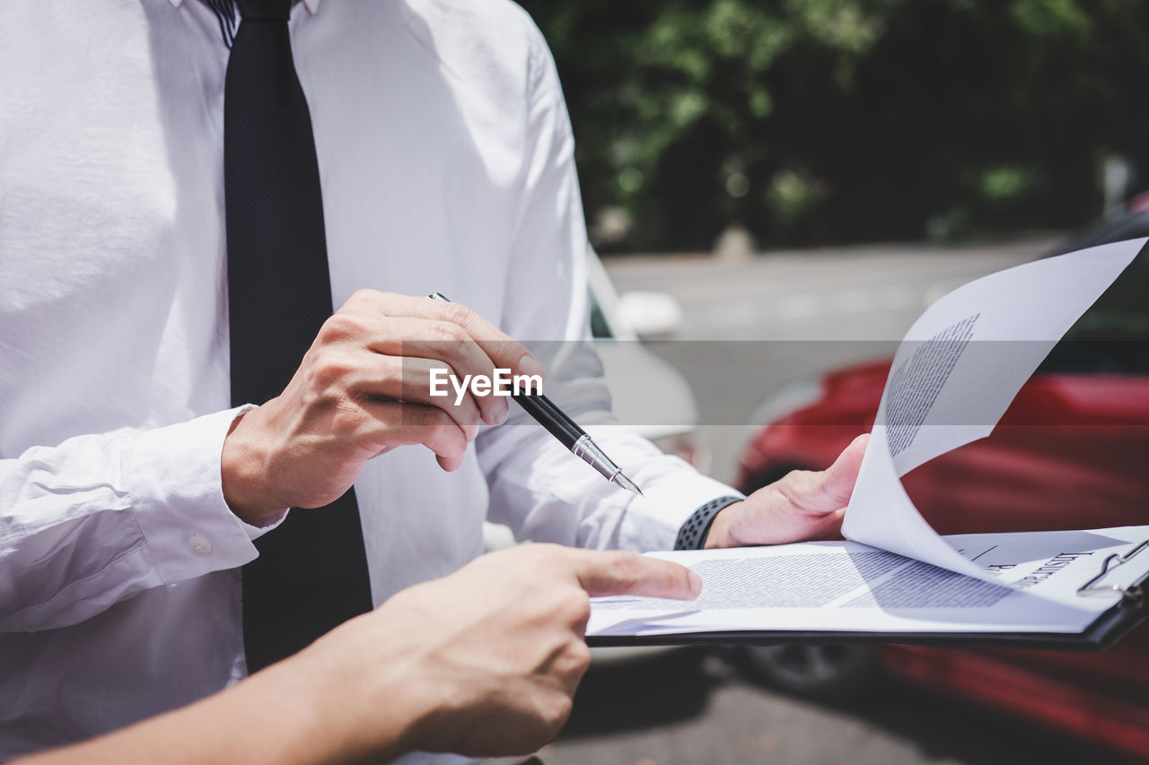 Midsection of customer pointing at contract while insurance agent holding clipboard