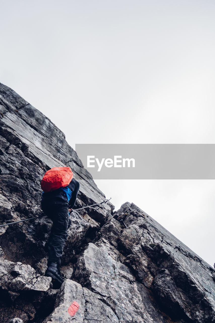 Low angle view of woman climbing rock against clear sky