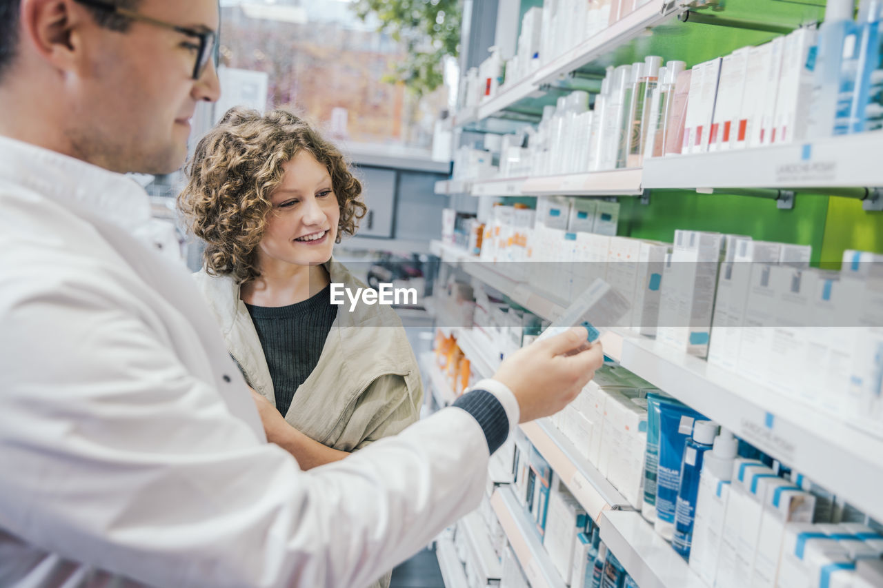 Pharmacist recommending medicine to smiling customer in chemist shop