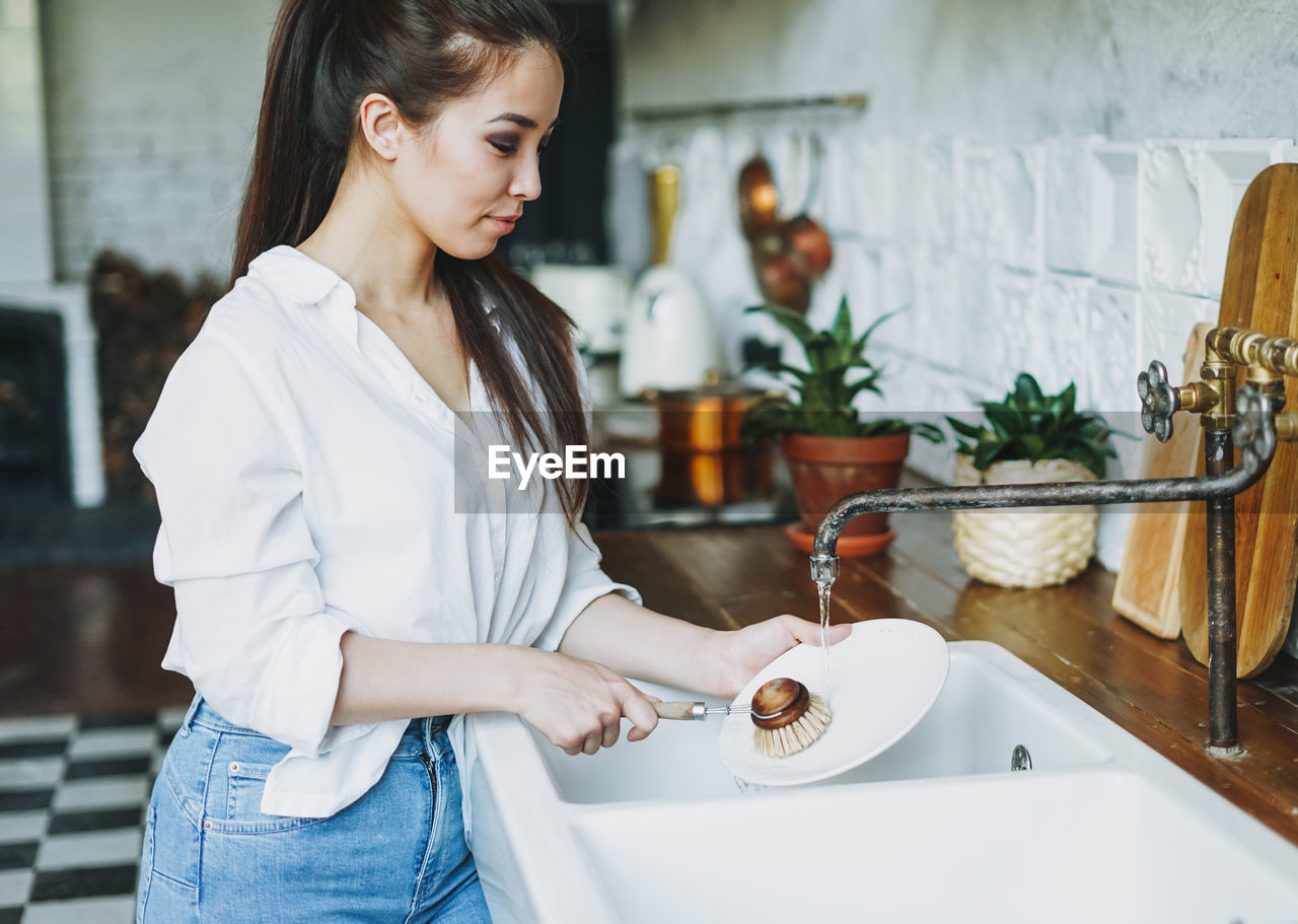 Young woman holding white while standing at home