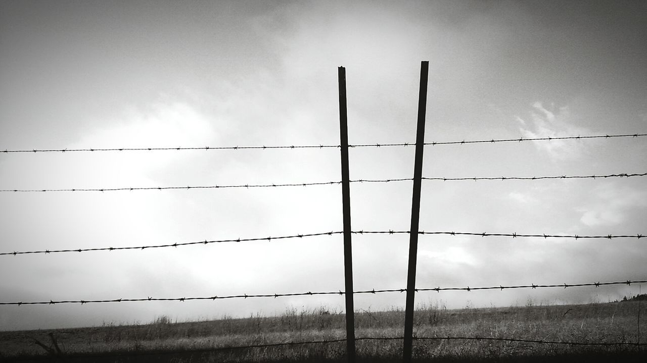 Barbed wire fence against sky on field