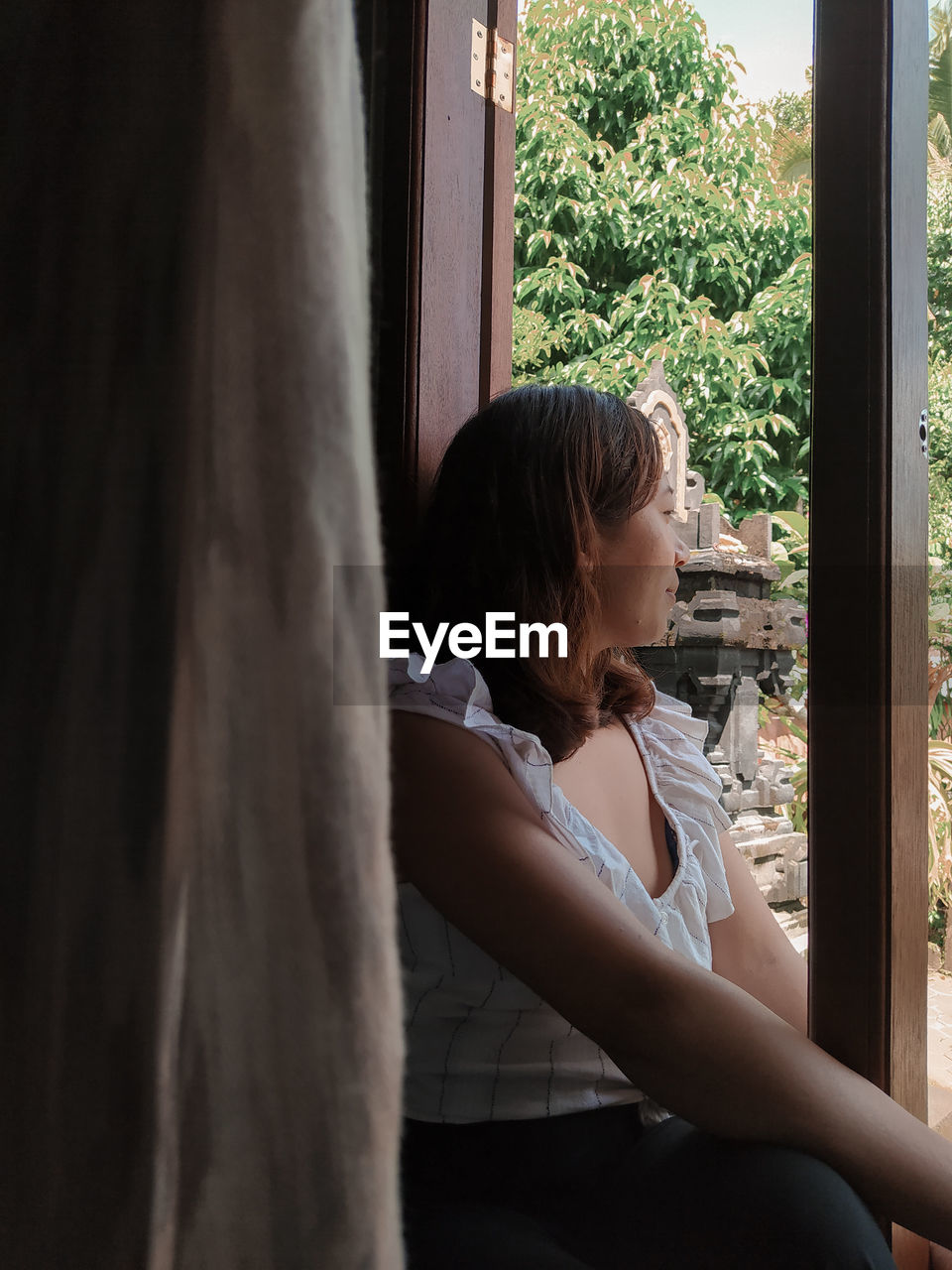 YOUNG WOMAN LOOKING THROUGH WINDOW AT HOME