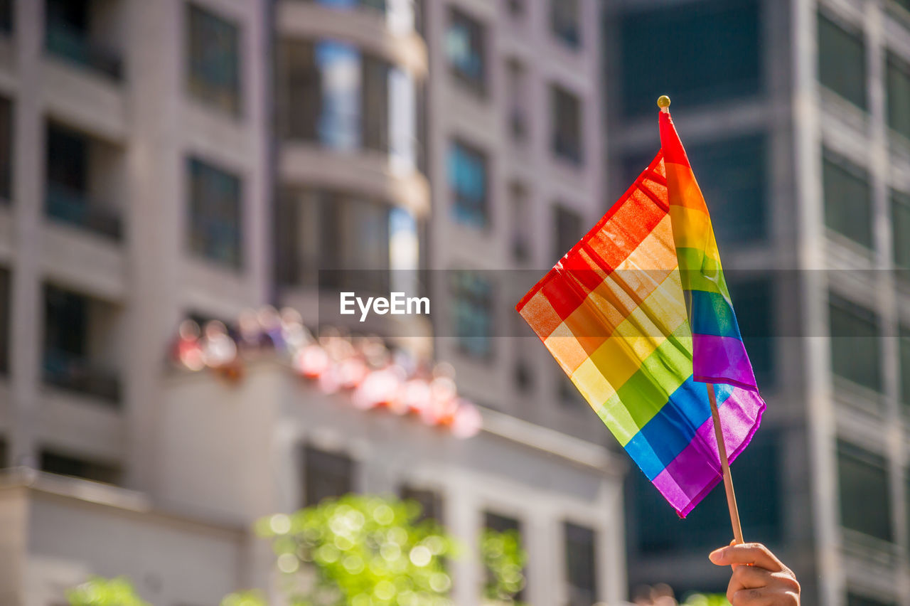 Cropped hand holding rainbow flag in city