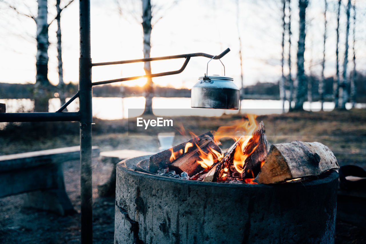Cozy campfire with bright flame heating metal pot in woods in winter at sunset