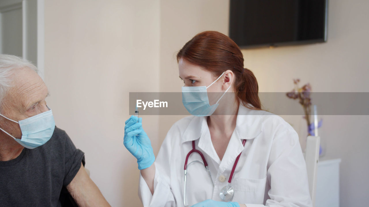 Doctor wearing mask vaccinating senior patient