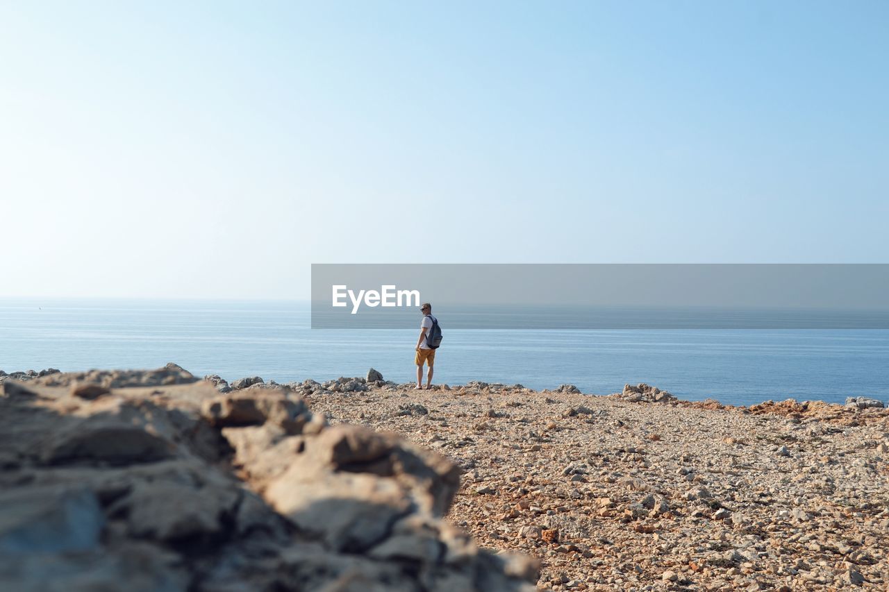 Man with backpack standing at beach against clear sky