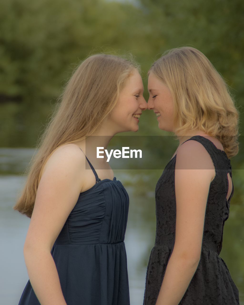 Side view of female friends rubbing noses while standing against lake