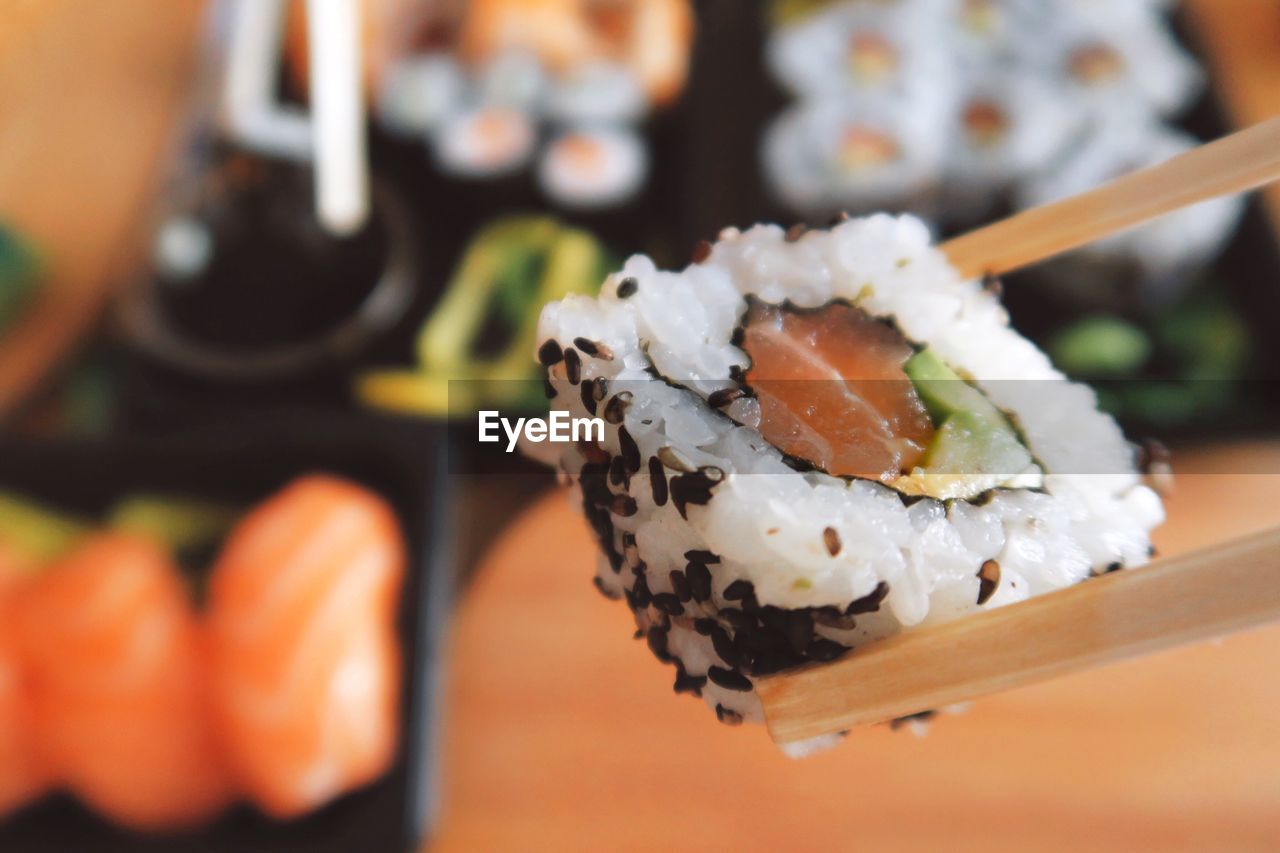 Close-up of chopsticks holding sushi roll over table