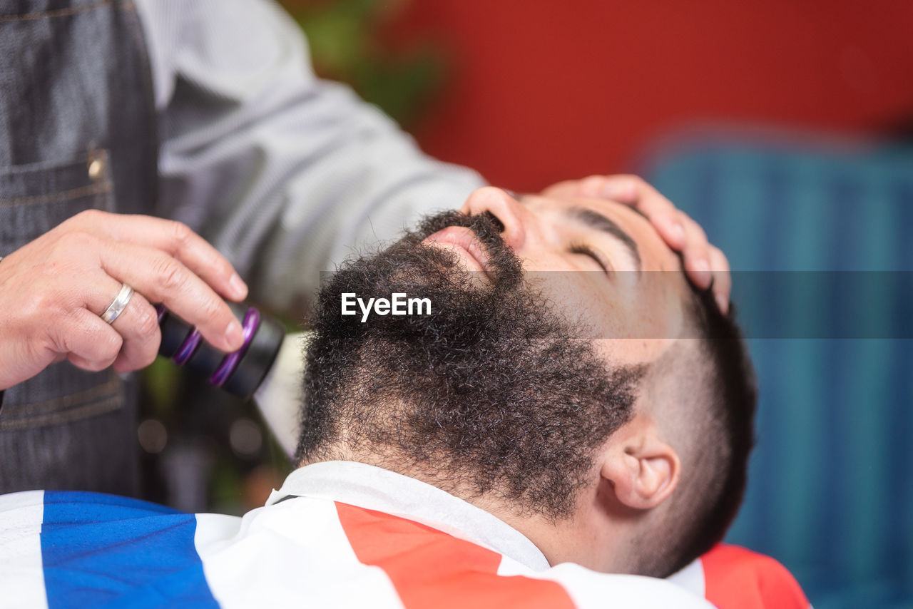 Midsection of barber shaving male customer hair in salon