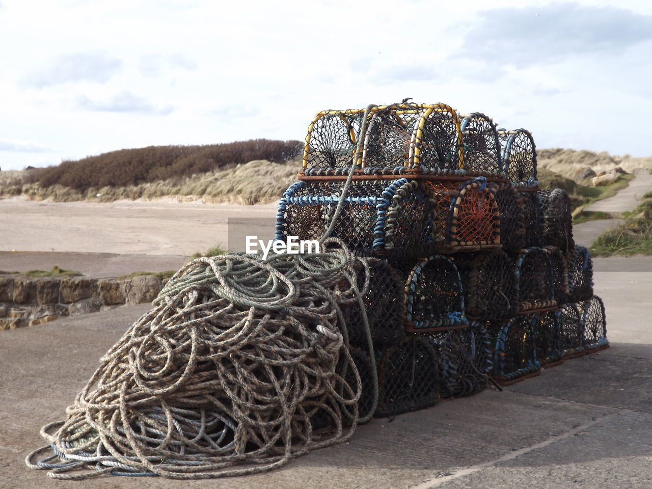 Stack of crab pots and ropes at beach against sky