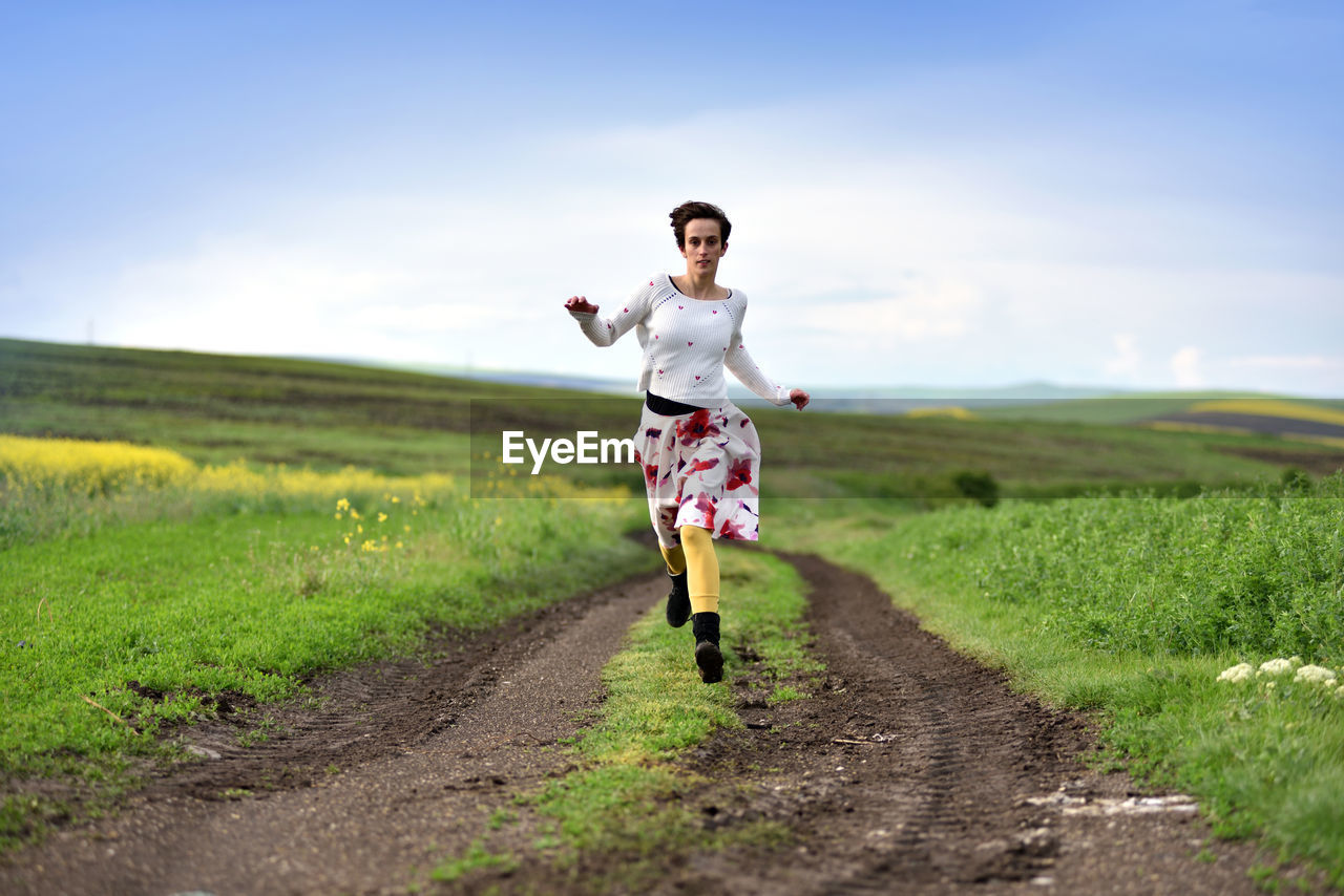 Portrait of young man running on field against sky