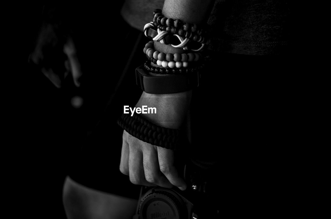 Midsection of person wearing bracelets against black background