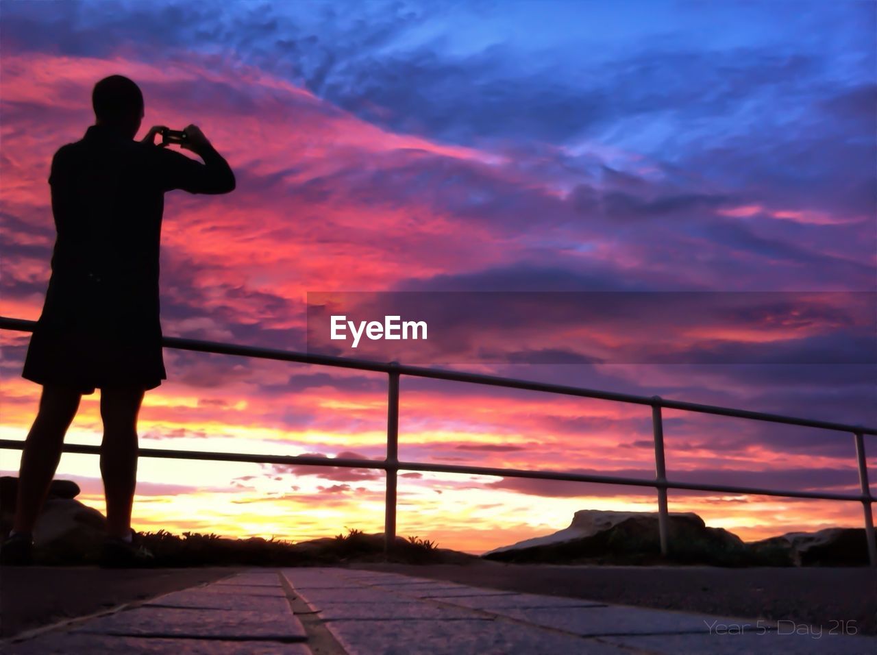 Silhouette man photographing cloudy sky at sunset