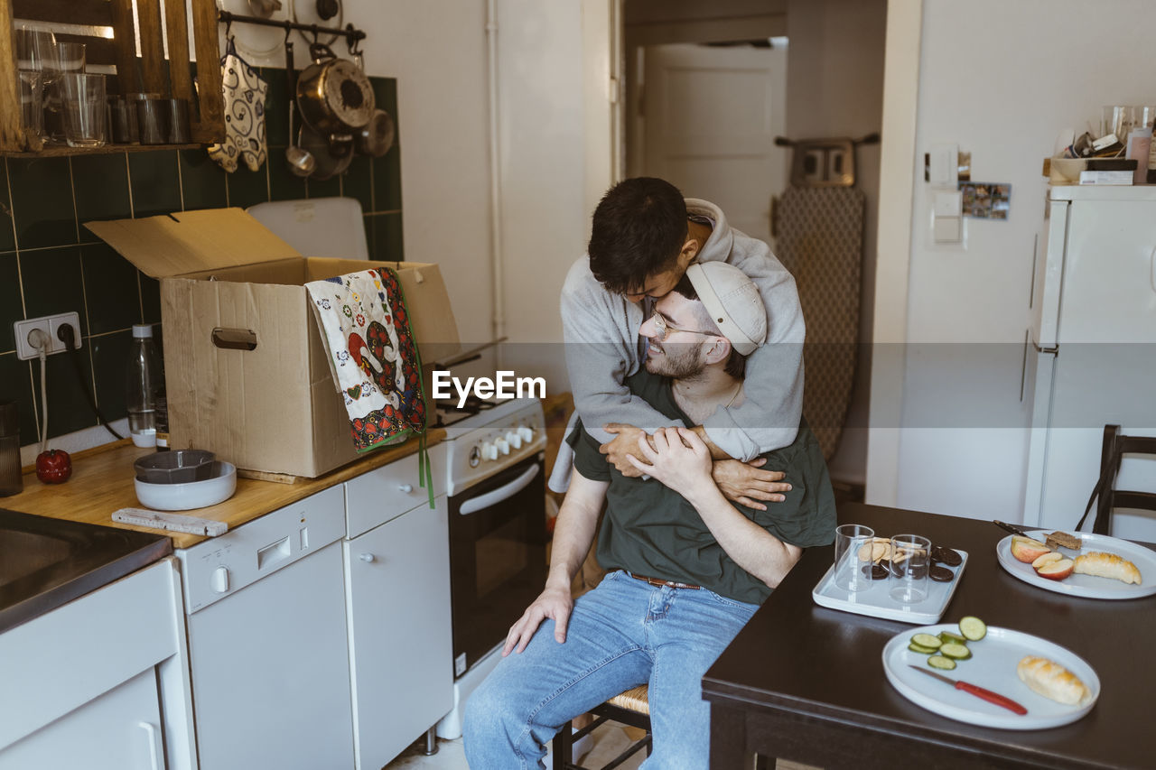 Romantic man embracing boyfriend in kitchen at home