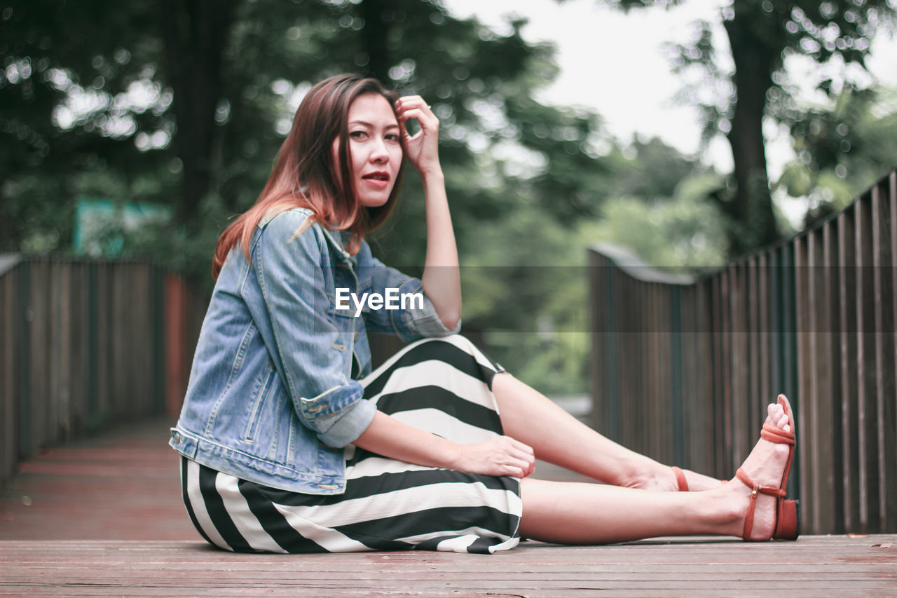 PORTRAIT OF YOUNG WOMAN SITTING ON FLOOR