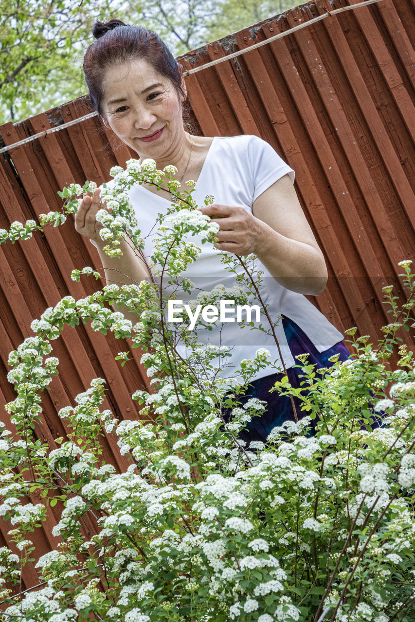 REAR VIEW OF WOMAN STANDING BY FLOWERING PLANTS