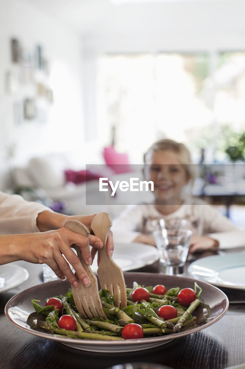 Cropped image of woman serving salad at dining table