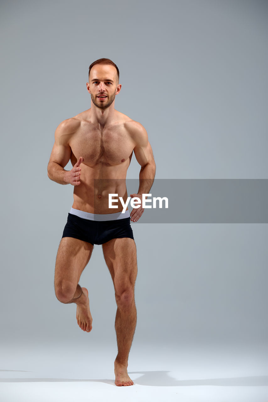 portrait of shirtless young man exercising against white background